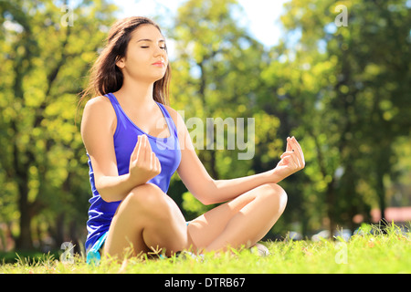 Giovane atleta femminile in sportswear meditando seduto su un prato verde in un parco Foto Stock