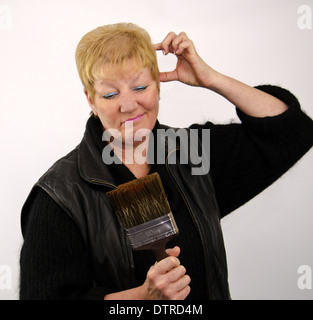 Capelli biondi donna che guarda perplesso con spazzola di vernice Foto Stock