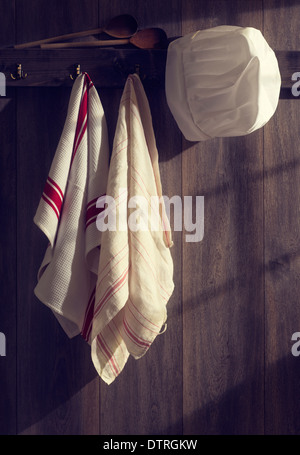 Chef hat con tè asciugamani appeso alla parete della cucina con lo streaming di luce solare attraverso la finestra Foto Stock