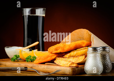 Il tradizionale pesce e patatine confezionate in carta con bevande di cola Foto Stock