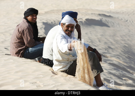 I beduini in appoggio sulla sabbia durante la gita turistica di portando i turisti sui cammelli a Douz,Sahara,Tunisia. Foto Stock