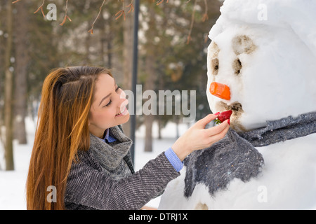 Ragazza giovane e carina a giocare con un pupazzo di neve Foto Stock