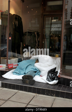 Una persona senza dimora nella foto dorme in un negozio di abbigliamento porta nel centro di Brighton, East Sussex, Regno Unito. Foto Stock