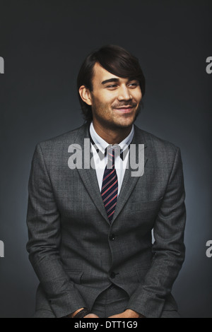 Ritratto di bel giovane imprenditore che guarda lontano sorridente. Attraente modello maschile in tuta su sfondo nero. Foto Stock