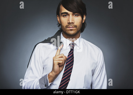 Ritratto di attraente giovane imprenditore tenendo il suo mantello sulla spalla. Rilassata business executive contro uno sfondo grigio. Foto Stock