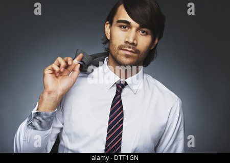 Ritratto di giovane attraente uomo in abbigliamento formale in posa contro uno sfondo grigio. Giovane imprenditore tenendo la sua giacca. Foto Stock