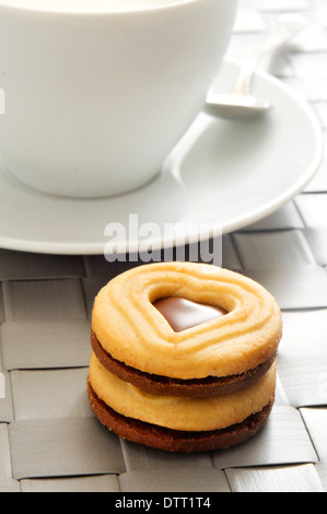 Primo piano di una tazza di latte e una pila di biscotti con cuore di un foro sagomato in un set tavolo per la prima colazione Foto Stock