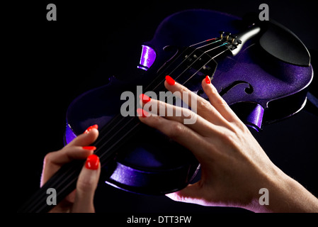 La signora con le mani di colore rosso brillante con le unghie su un violino viola Foto Stock