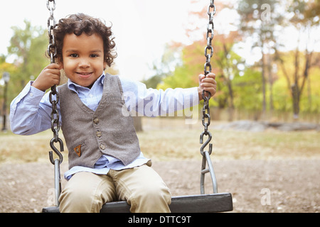 Razza mista ragazzo seduto su swing in posizione di parcheggio Foto Stock