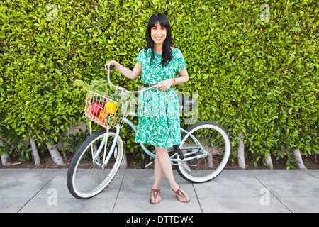 Donna che trasportano produrre in bicicletta paniere Foto Stock