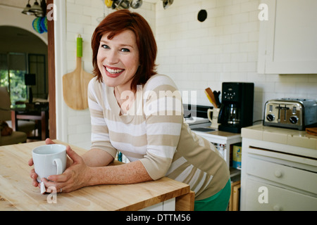 Incinta donna caucasica bicchiere di tè in cucina Foto Stock