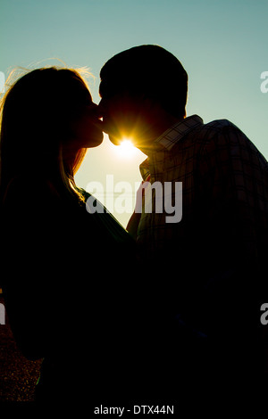 Giovane baciare con sun flare proveniente in sotto la loro i menti di sera. Foto Stock