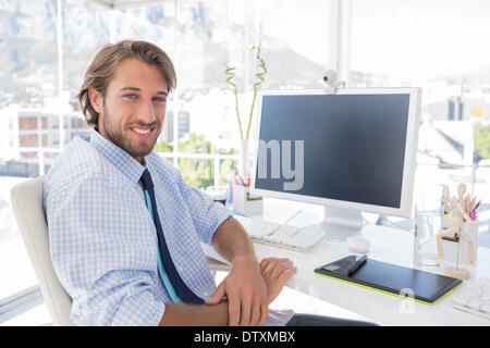 Designer sorridente seduto alla sua scrivania Foto Stock