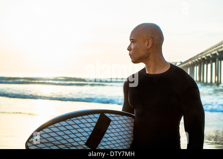 Razza mista uomo con la tavola da surf in spiaggia Foto Stock