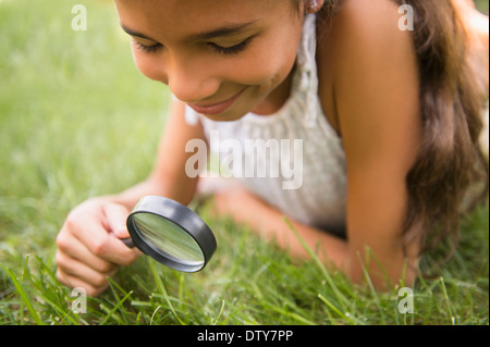 Razza mista ragazza con lente di ingrandimento in erba Foto Stock