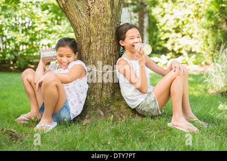 Razza mista ragazze parlando in barattolo di latta telefoni all'aperto Foto Stock