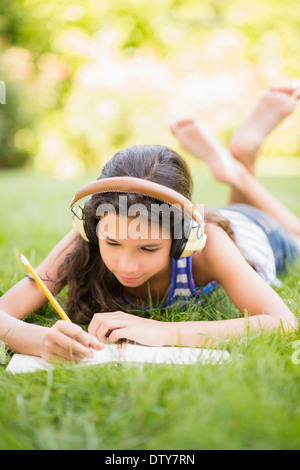 Razza mista ragazza ascoltando le cuffie e il disegno all'aperto Foto Stock