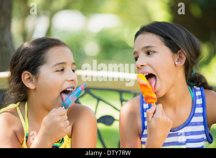 Razza mista ragazze mangiare ghiaccio aromatizzato all'aperto Foto Stock