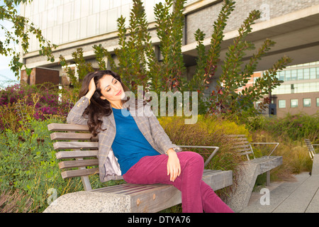 Razza mista donna seduta su una panchina nel parco Foto Stock