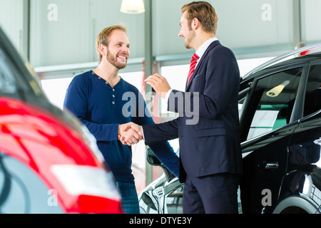 Venditore o venditore auto e del cliente in concessionaria, si stringono le mani, consegna le chiavi della macchina Foto Stock