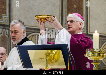 Il vescovo Noel Treanor contiene una piastra di oro con fette di pane durante la messa. Foto Stock