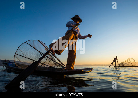 Pescatori nella luce della sera, gamba rematori con un tradizionale cestello sul loro canoe, tramonto al Lago Inle, Stato Shan, Myanmar Foto Stock
