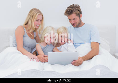 Bella famiglia usando un computer portatile a letto Foto Stock