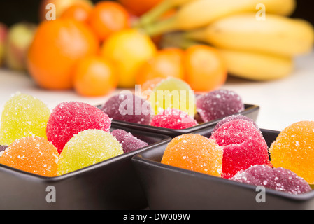 Colorato gelatine di frutta in little black tazze di ceramica. Frutti in background Foto Stock