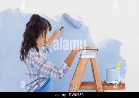 Donna che utilizza il rullo di vernice alla parete di vernice Foto Stock