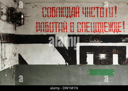 Milovice, Repubblica Ceca. Il 25 febbraio 2014. Era sovietica segni "TENERLO PULITO!' e 'indossare tuta!' in russo sulla parete di un edificio abbandonato nella zona del militare sovietica in base Milovice, situato a circa 40 km da Praga, Repubblica Ceca. Rovine della ex Unione Sovietica base militare in Milovice sono per essere demolita nei prossimi mesi per fare spazio a nuovi edifici. La base è stata abbandonata per più di venti anni, dal momento che le truppe sovietiche a sinistra della Cecoslovacchia nel 1991. Ora il abbandonata base militare sopravvive per ultimi giorni. Foto Stock