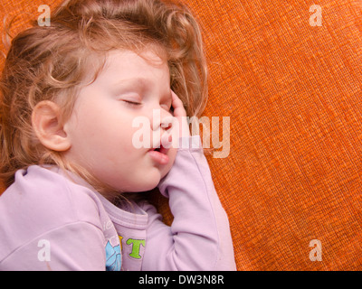 Una bambina di tre anni che dorme sul divano, mettendo una mano sotto la sua testa Foto Stock