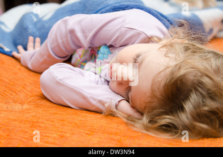 Una bambina di tre anni che dorme sul divano, mettendo una mano sotto la sua testa Foto Stock