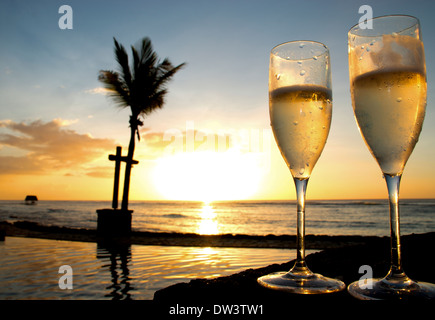 Due bicchieri di champagne o vino frizzante accanto ad una piscina con il sole tramontare sull'oceano Foto Stock