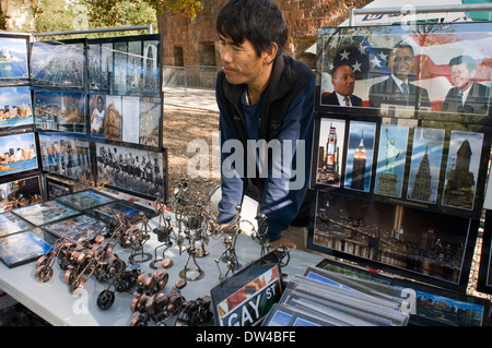 Un uomo che sta dietro una grande mostra di foto, segni e altri souvenir di New York a Battery Park. Venditore a vendere cartoline Foto Stock