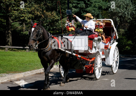 Carro trainato da cavalli con i turisti a bordo di Central Park di New York STATI UNITI D'AMERICA in primavera. Central Park. Equitazione. Piazza del nord è dominato dalla golden statua equestre del generale William Tecumseh Sherman, condotta nel 1903 dallo scultore Augustus Saint-Gaudens. Questo è il più usato ingresso al Central Park e il luogo dove si possono noleggiare un cavallo carrello per giro attorno al parco. Foto Stock