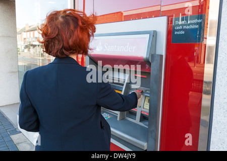 Persona inserendo una carta in un bancomat presso una banca Santander per fare un ritiro di contanti, Nottinghamshire, England, Regno Unito Foto Stock