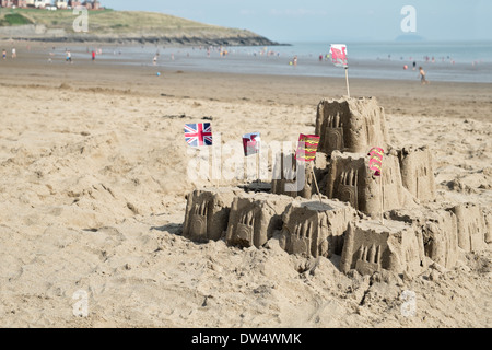 Un castello di sabbia su una spiaggia di gallese con il mare alle spalle e vacanzieri godere l'acqua Foto Stock