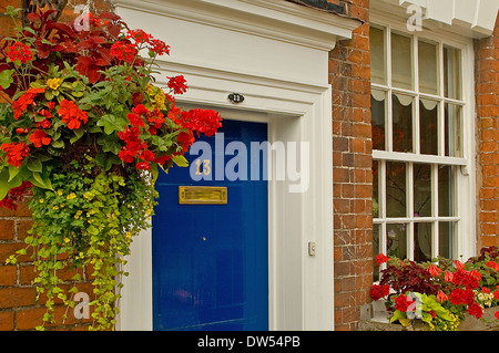 Porta blu con cornice bianca, ottone letter box, numero tredici e appendere il cestello con fiori di colore rosso e nella finestra casella. Foto Stock