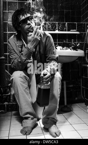 Uomo ubriaco si siede in una toilette di bere whisky e fumatori Foto Stock