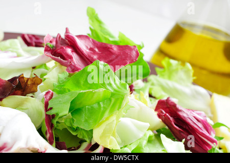 Ingrandimento di una piastra con mesclun, un mix assortiti di foglie di insalata, su un set tavolo con una bottiglia di olio di oliva Foto Stock