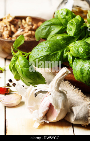Mazzetto di basilico fresco, tazza di noci, pepe e aglio servita su bianco tavolo in legno. Vedere serie Foto Stock