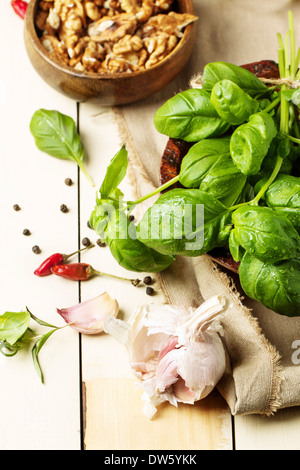 Mazzetto di basilico fresco, tazza di noci, pepe e aglio servita su bianco tavolo in legno. Vedere serie Foto Stock