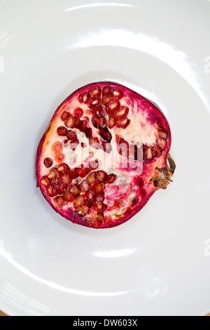 Melograno frutta tagliata a metà longitudinalmente su una piastra bianca Foto Stock