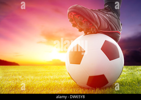 Il calcio o il pallone da calcio al calcio di inizio di un gioco con il tramonto del sole Foto Stock