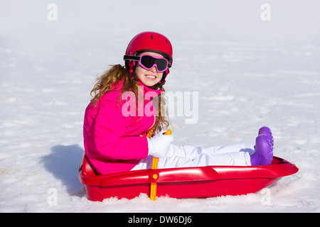 Kid girl giocare sled in inverno la neve con casco ang gli occhiali di protezione Foto Stock