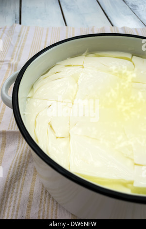 Freschi Fatti in casa il formaggio bianco in un contenitore con acqua salina Foto Stock