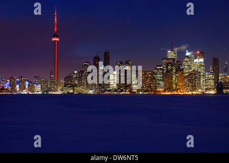 Blu crepuscolo ora dalla coperta di neve congelati Lago Ontario di Toronto skyline della città si illumina di notte in inverno Foto Stock