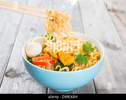 Il curry piccante tagliatelle istante con bacchette. Cucina asiatica, pronti a servire sul tavolo da pranzo in legno impostazione. Fresca con caldo cotto a vapore di fumo. Foto Stock