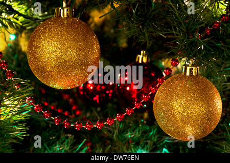 Due oro scintillante palla Natale ornamenti sull'albero. Con il rivestimento rosso e palle rosse, vacanza festosa decorazioni. Foto Stock
