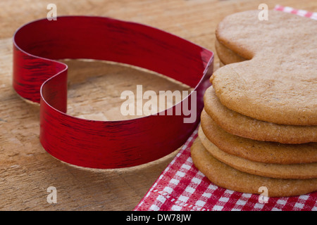 Rosso a forma di cuore cookie cutter e una pila di marrone in casa natale gingerbreads rustico sfondo di legno Foto Stock